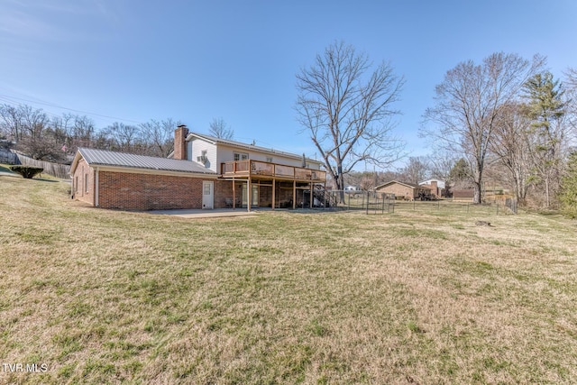 rear view of property with brick siding, metal roof, a lawn, and a wooden deck