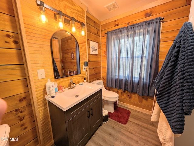 bathroom featuring visible vents, toilet, wood finished floors, vanity, and wood walls