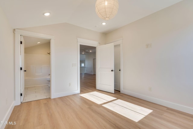 unfurnished bedroom with lofted ceiling, baseboards, light wood finished floors, and ensuite bathroom