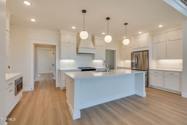 kitchen with white cabinets, custom range hood, appliances with stainless steel finishes, light countertops, and a sink