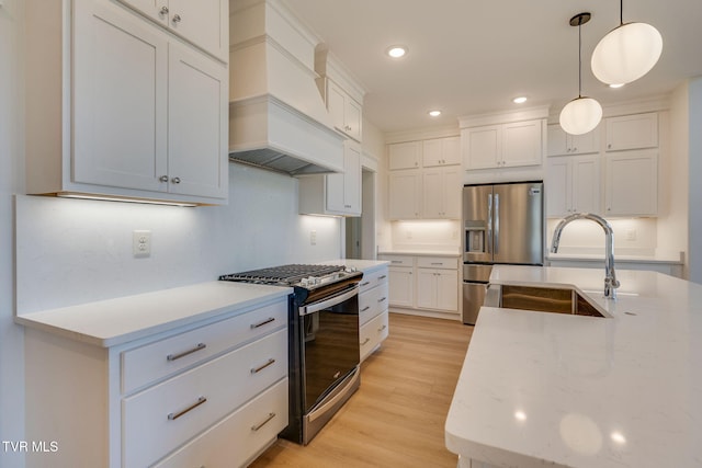 kitchen featuring custom range hood, decorative light fixtures, stainless steel appliances, light wood-style floors, and a sink