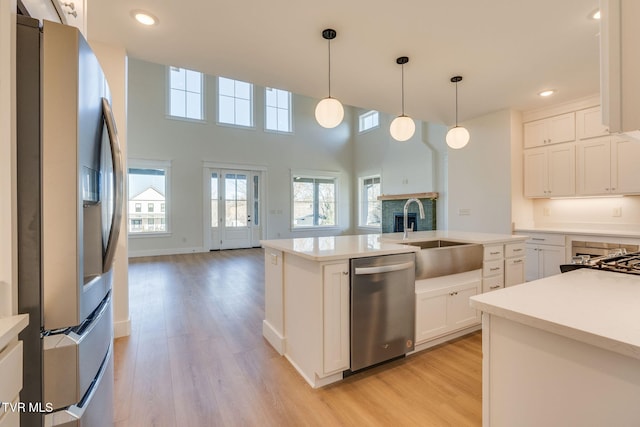 kitchen featuring light wood-style flooring, a sink, open floor plan, light countertops, and appliances with stainless steel finishes