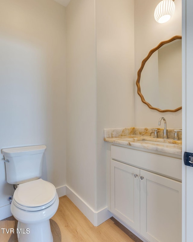 half bath with vanity, wood finished floors, toilet, and baseboards