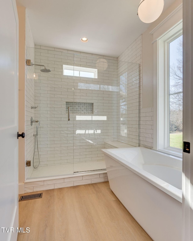 full bathroom with visible vents, wood finished floors, a bath, and a shower stall