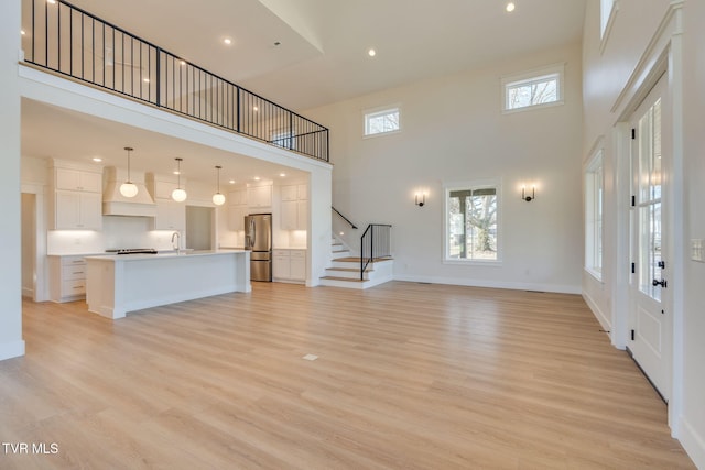 unfurnished living room with light wood-style floors, stairway, a sink, and a healthy amount of sunlight