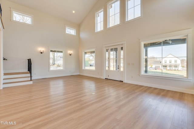 unfurnished living room featuring stairs, high vaulted ceiling, baseboards, and light wood-style floors