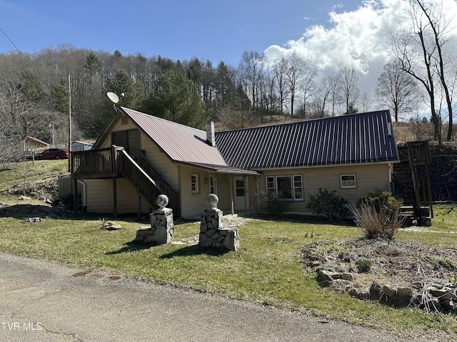 view of front of house featuring a chimney, stairway, metal roof, and a front yard