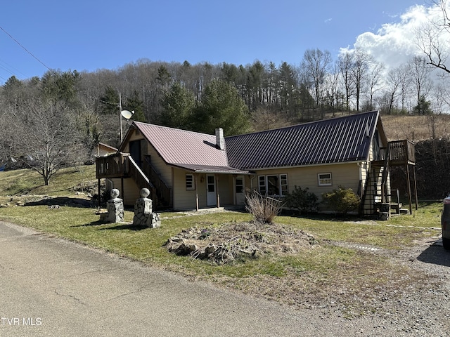 view of front of property featuring stairway, a view of trees, metal roof, and a wooden deck