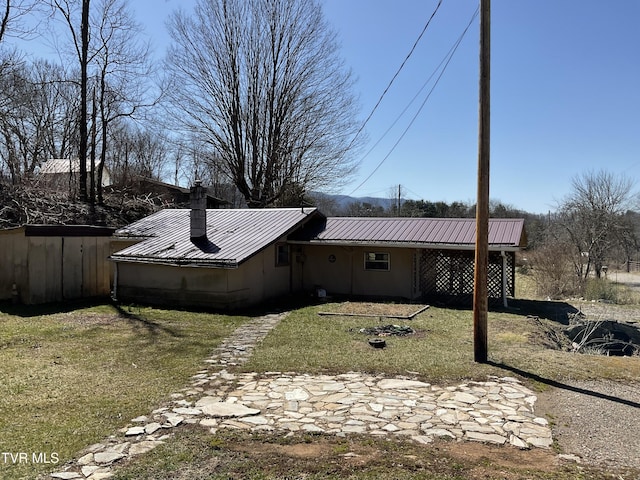 back of property with a chimney, metal roof, and a yard