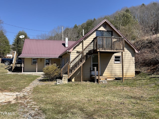 back of property featuring metal roof, a lawn, and stairs