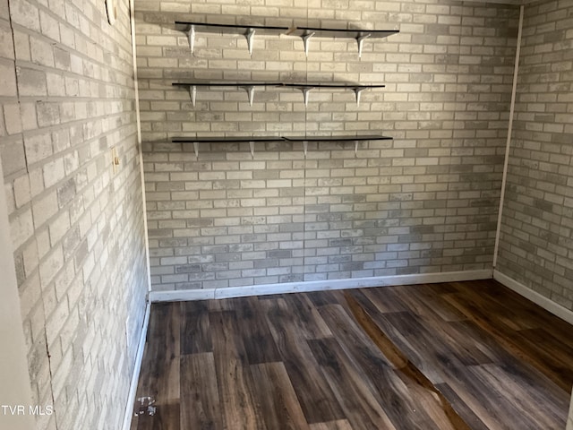 empty room featuring brick wall, dark wood-type flooring, and baseboards