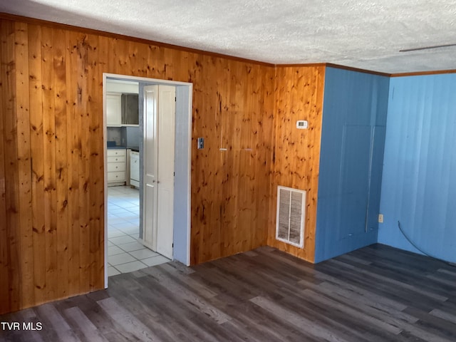 spare room featuring wood finished floors, visible vents, ornamental molding, wood walls, and a textured ceiling