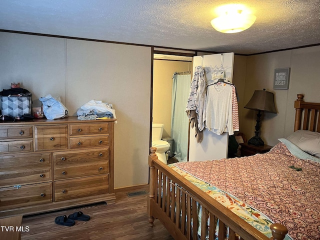 bedroom featuring ornamental molding, a textured ceiling, ensuite bath, and wood finished floors