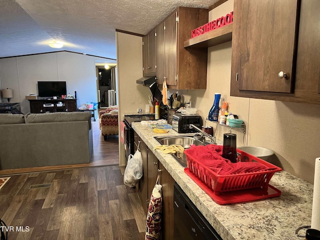 kitchen featuring a textured ceiling, under cabinet range hood, dark wood-type flooring, vaulted ceiling, and light countertops