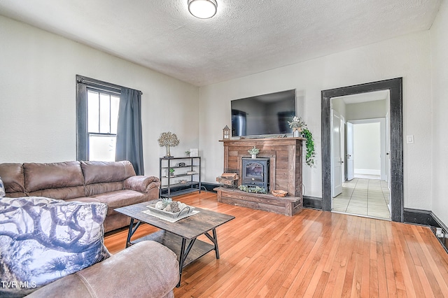 living room with a textured ceiling, wood-type flooring, a wood stove, and baseboards