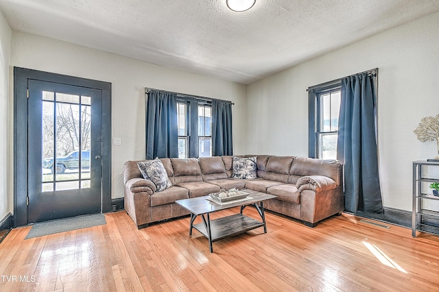 living area featuring a textured ceiling, light wood-type flooring, and a healthy amount of sunlight