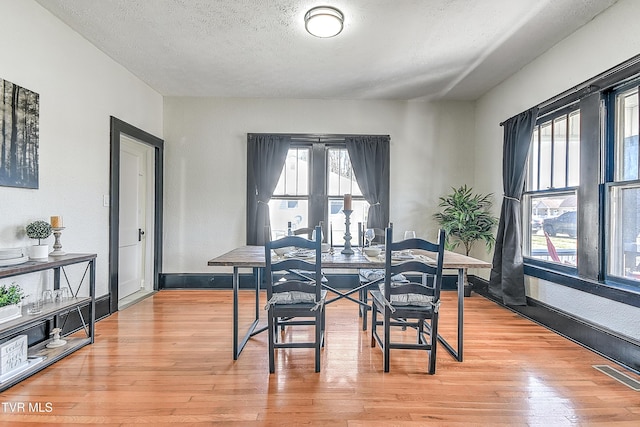 dining room with a textured ceiling, a wealth of natural light, visible vents, and light wood-style floors