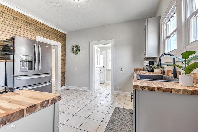 kitchen with butcher block countertops, light tile patterned flooring, a sink, and stainless steel fridge with ice dispenser