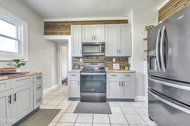 kitchen featuring a textured ceiling, appliances with stainless steel finishes, light tile patterned flooring, and backsplash