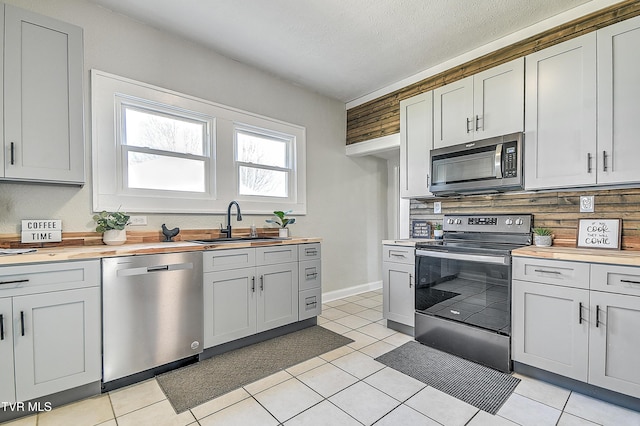 kitchen with light tile patterned floors, appliances with stainless steel finishes, wooden counters, and a sink