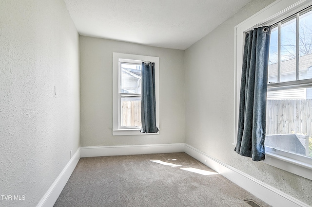 carpeted empty room featuring visible vents, baseboards, a textured ceiling, and a textured wall