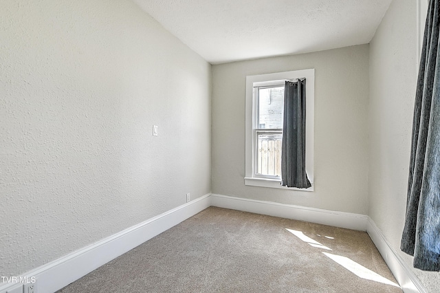 empty room featuring carpet floors, a textured wall, a textured ceiling, and baseboards