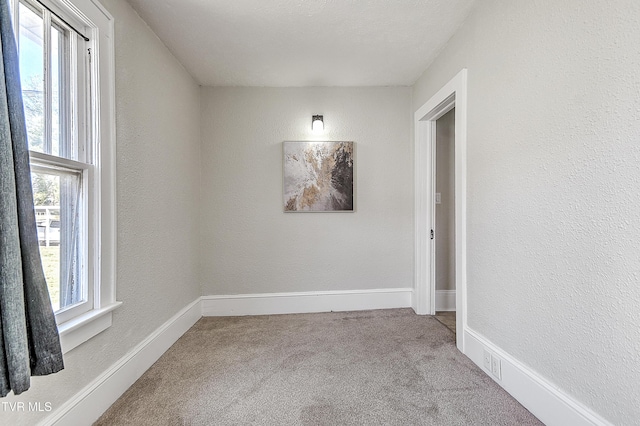 carpeted empty room with a textured wall and baseboards