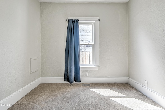 carpeted spare room with visible vents and a textured wall