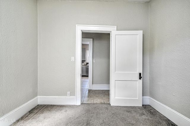 spare room featuring carpet, baseboards, and a textured wall