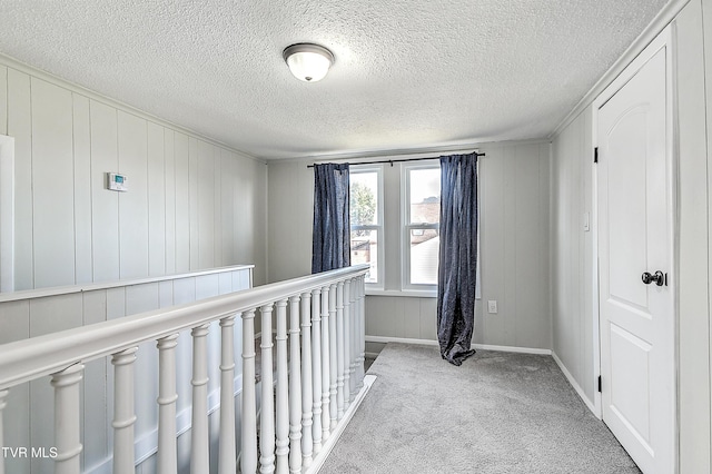 hall featuring baseboards, light colored carpet, a textured ceiling, and an upstairs landing