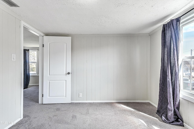 carpeted empty room featuring a textured ceiling, visible vents, and baseboards