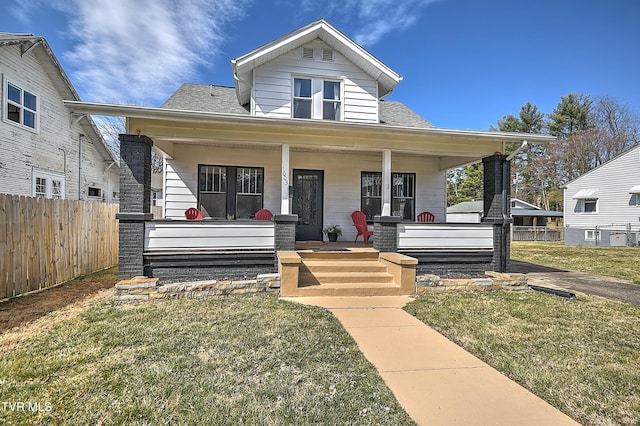 bungalow-style house with covered porch, fence, a front lawn, and roof with shingles