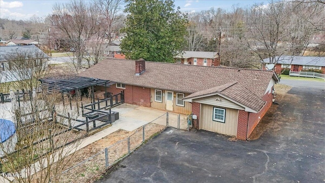 view of front of property with a shingled roof, brick siding, fence, and a chimney