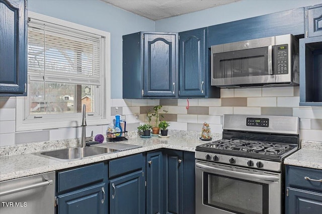 kitchen with appliances with stainless steel finishes, a sink, decorative backsplash, and blue cabinetry