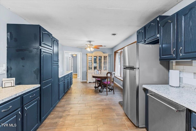 kitchen with appliances with stainless steel finishes, blue cabinets, light countertops, and light wood finished floors