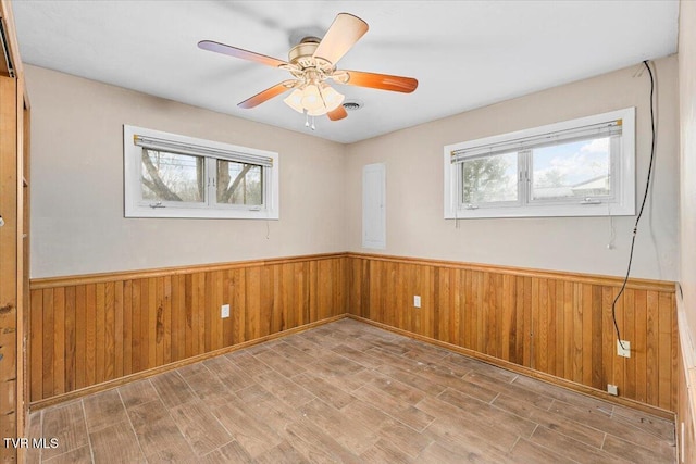 empty room with a ceiling fan, a wainscoted wall, wooden walls, and wood finished floors