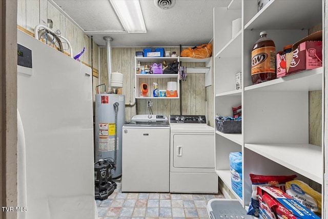 washroom featuring water heater, visible vents, wooden walls, laundry area, and independent washer and dryer