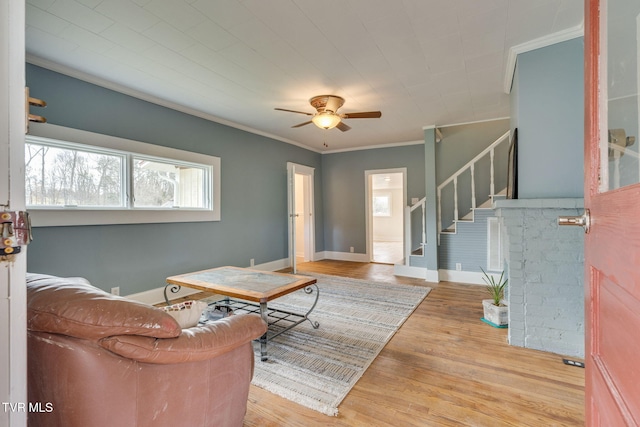 living area featuring baseboards, ceiling fan, ornamental molding, wood finished floors, and stairs