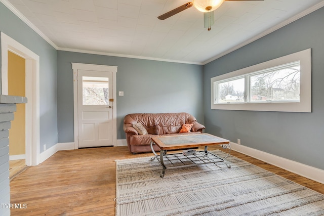 living area featuring light wood finished floors, ceiling fan, baseboards, and crown molding