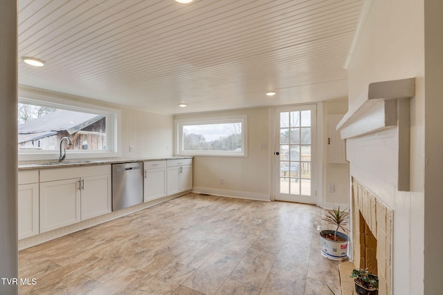 kitchen with light stone counters, white cabinetry, a sink, dishwasher, and baseboards