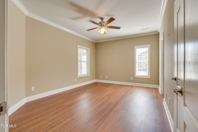 empty room featuring baseboards, wood finished floors, visible vents, and crown molding