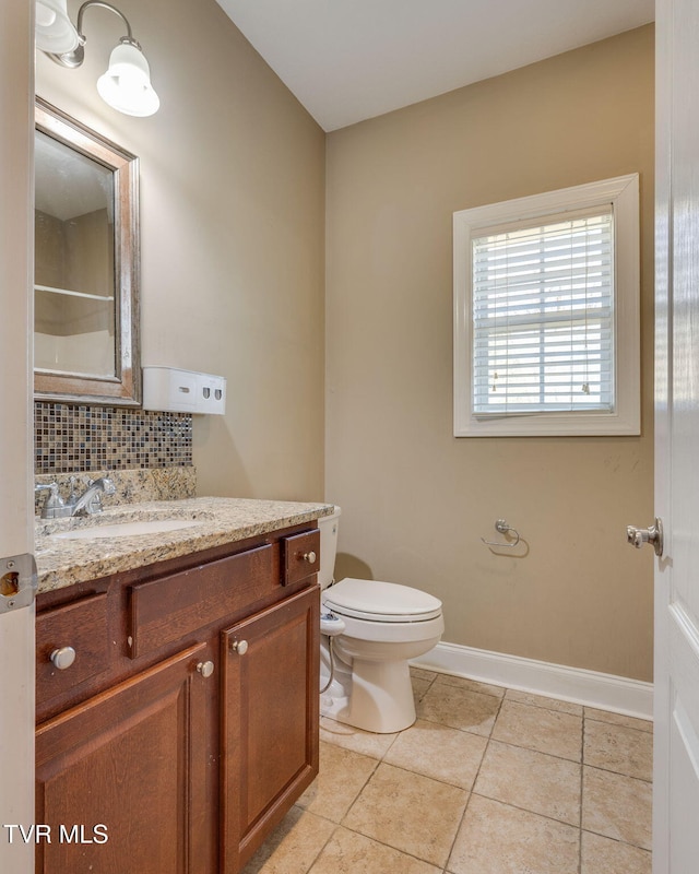 bathroom featuring tasteful backsplash, toilet, vanity, baseboards, and tile patterned floors