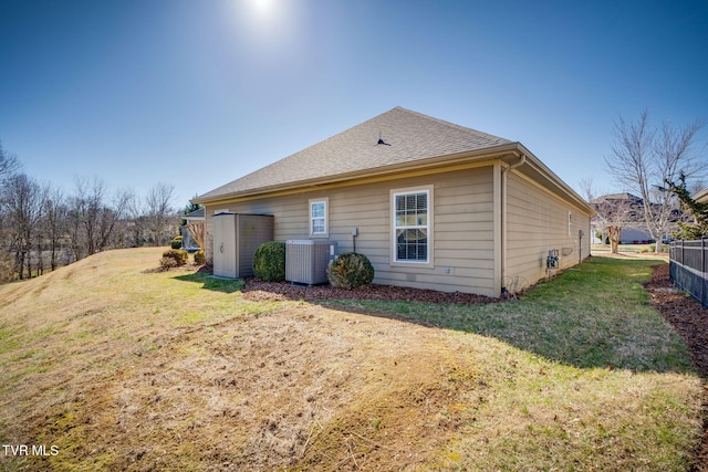 rear view of house with roof with shingles, a yard, fence, and central air condition unit