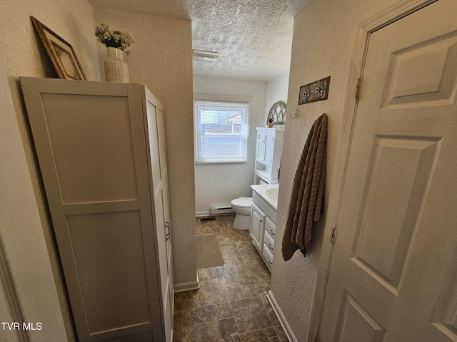 bathroom featuring toilet, baseboard heating, a textured ceiling, and a textured wall