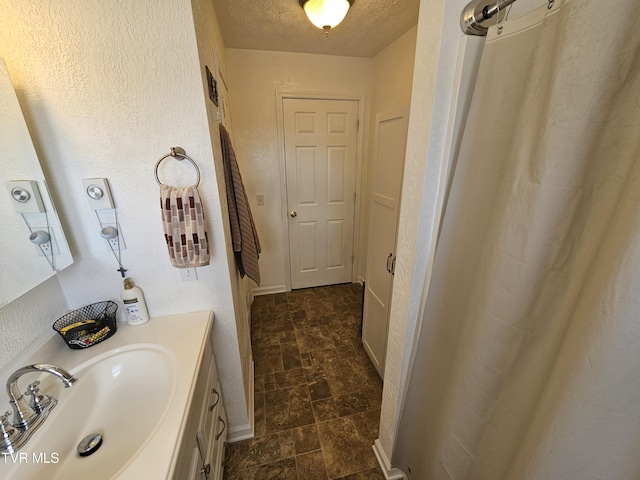 full bathroom with baseboards, a textured wall, stone finish floor, a textured ceiling, and vanity