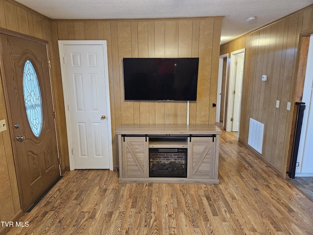 entryway with ornamental molding, wood walls, wood finished floors, and visible vents