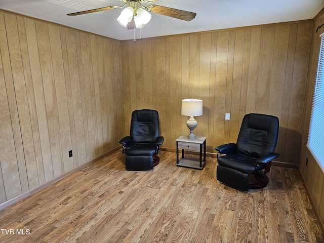 living area with wood finished floors, a ceiling fan, and wooden walls