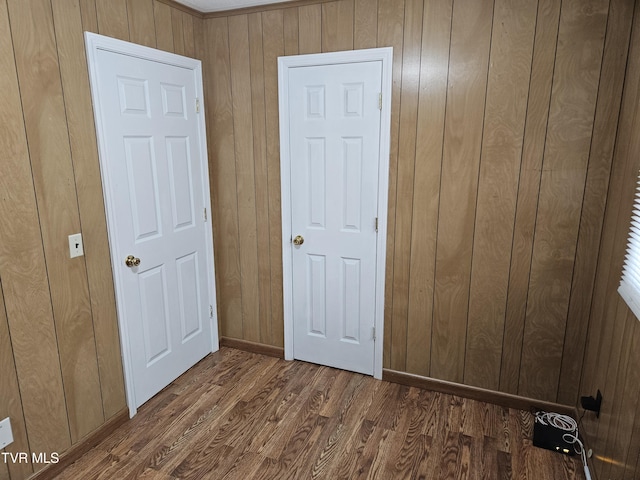 unfurnished bedroom with wooden walls, baseboards, and wood finished floors