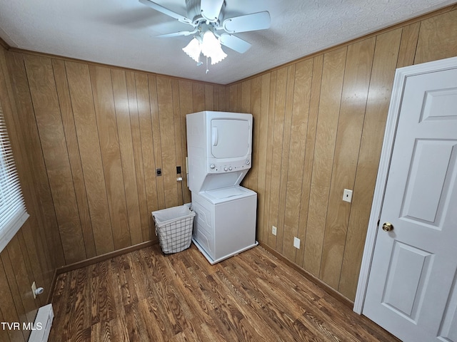 laundry area with stacked washer and dryer, ceiling fan, wood walls, wood finished floors, and laundry area