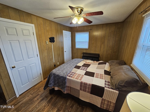 bedroom with a textured ceiling, wood finished floors, a ceiling fan, and wooden walls